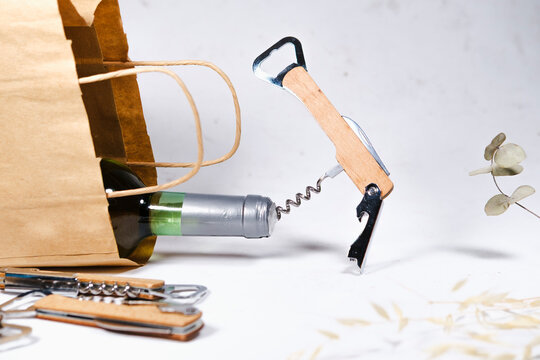 wooden bottle opener, corcscrew with switchblade, bottle of wine in eco craft paper bag on white background, commercial photo concept