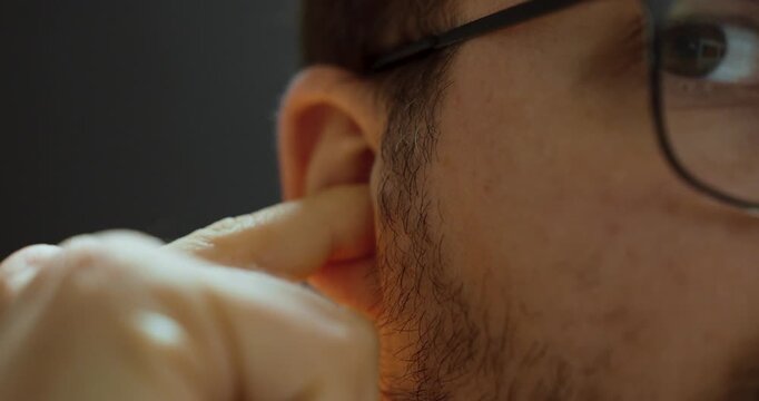 Close-up of a man putting earplugs into his ears, symbolizing workplace safety, hearing protection, and health awareness.