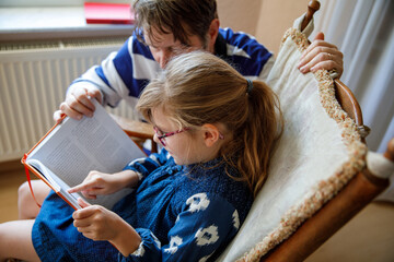 Little girl and father read book at home. Happy child with eyeglasses and man reading. Education for children, family time