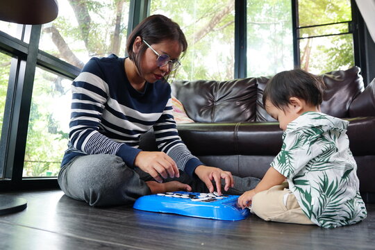 A woman wearing glasses is sitting on the floor playing checkers or a similar board game with a small child in a living room.