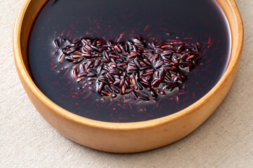 Black rice and rice water are placed in a handmade wooden tray on a linen table.