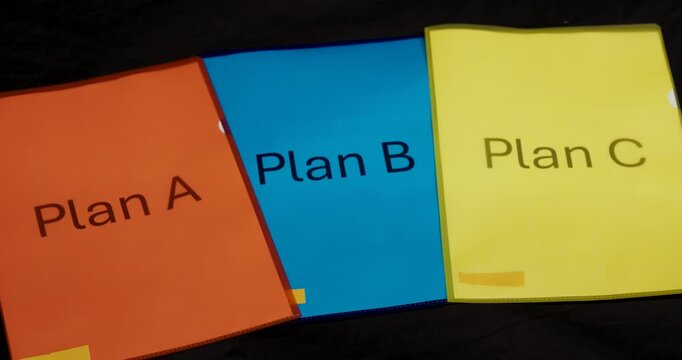 Three folders labeled Plan A, Plan B, and Plan C lie on a table. One plan is selected and removed from the scene, symbolizing decision-making and strategy.