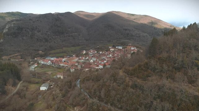 High aerial clip coming back from valley towards Isaba village during cloudy day with sunrays in mountain background.