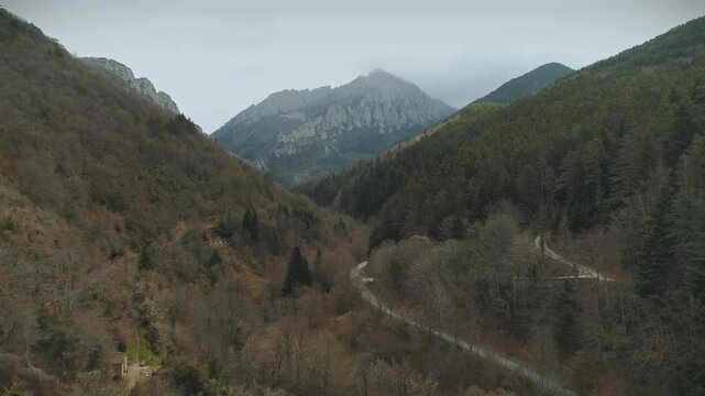 Forward drone flight through a gorge in Isaba mountain range with a walking path below and early spring-colored trees.
