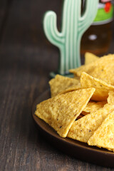 A plate of nachos chips sits on a dark wooden table, with a stylized cactus in the background. The image captures the essence of a casual and fun snack or appetizer.