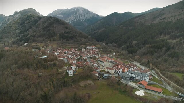 Drone approach towards Isaba village with mountains in the background and early spring colors on cloudy day.