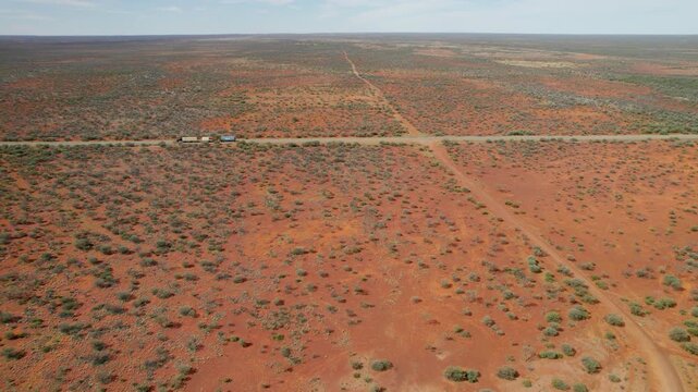High aerial shot of a roadtrain driving along the Stuart Highway, surrounded by Australia&rsquo;s deep red desert. The wide open landscape and long straight road highlight the scale of the outback.