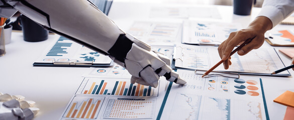 A captivating image depicting a human hand and a robotic arm collaborating on data analysis in a modern office, emphasizing teamwork and technology integration.Noogenesis