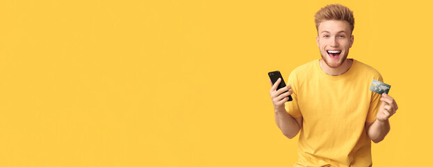 Happy young man with credit card and mobile phone on color background