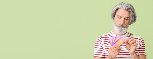 Senior man with gift cards on color background