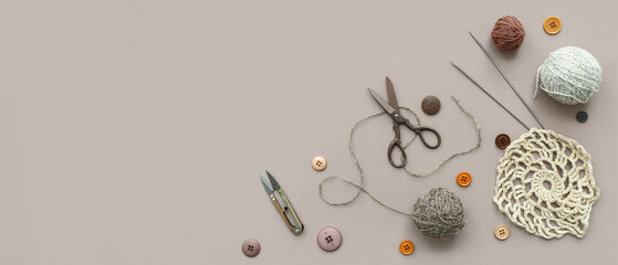 Knitting needles, yarn balls and buttons on grey background