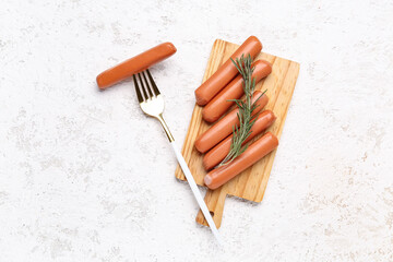 Wooden board with tasty sausages on light background