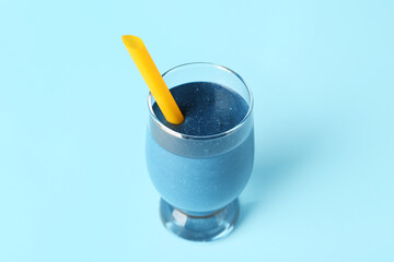 Glass of tasty blue smoothie with straw on color background