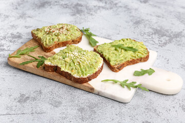 Board of tasty avocado toasts on light background
