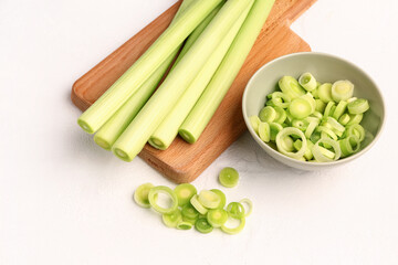 Board and bowl with slices of fresh leek on white background
