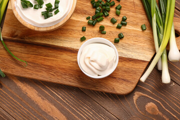 Bowls of tasty sour cream with sliced green onion on wooden background