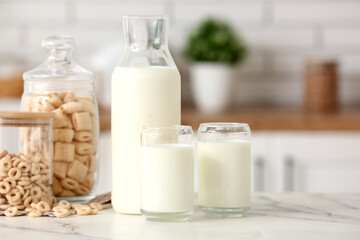 Glasses and bottle of fresh milk with cereal rings on white table