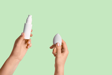 Female hands with makeup sponge and bottle of foundation on green background
