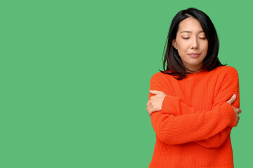 Young Asian woman hugging herself on green background