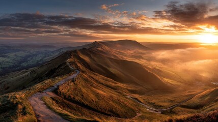 Golden sunrise over mam tor mountain ridge with glowing sky and rolling hills in the peak district, united kingdom creating a peaceful scenic landscape view