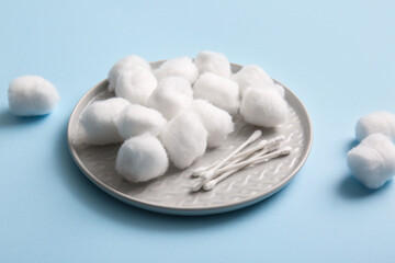 Plate with cotton balls and swabs on blue background