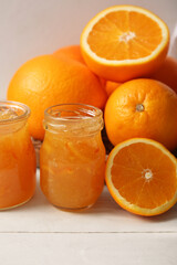 Jars of tasty orange jam on white wooden background