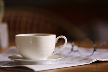 Newspaper with cup of coffee on table against blurred background, closeup