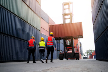 Three men in orange vests walk in front of a large container truck