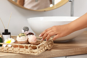Young woman with bath bombs and incense sticks near sink in bathroom, closeup