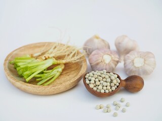 Several white peppercorns placed on a wooden spoon and garlic and coriander root placed on a white background. Healthy food seasononing. Three buddies.