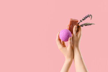 Female hands holding soap bar, bath bomb and lavender flowers on pink background, closeup