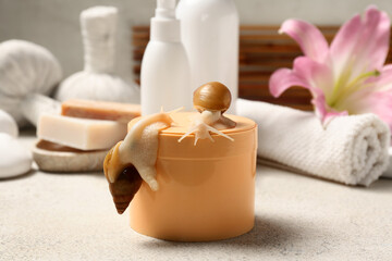 Jar of cosmetic product with Giant Achatina snails and spa accessories on light table