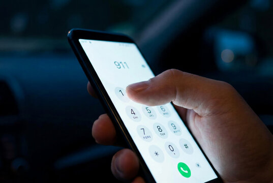Hand dialing 911 on smartphone inside car at night