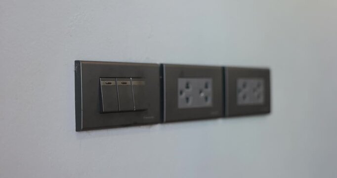 Close up shot of a hand press a black modern light switch on a gray wall next to multiple electrical outlets, symbolizing home power control and energy efficiency. 4K VDO