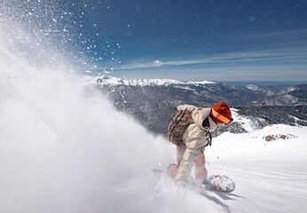 Fast man snowboarder rides in cloud of powder snow off-piste outside of ski slope. Backcountry freeride at ski resort concept