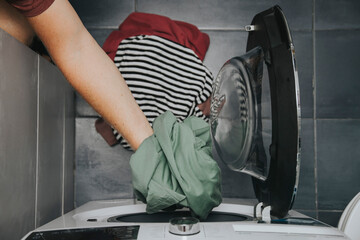 Hands putting dirty laundry in a front-loading washing machine.