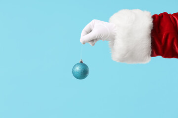 Fototapeta na wymiar Santa Claus holding shiny Christmas ball on color background, closeup