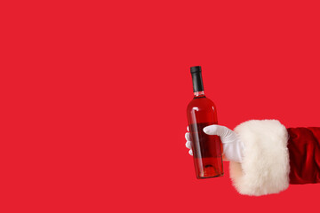 Santa Claus holding bottle of wine on red background