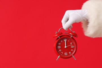 Santa Claus holding alarm clock on red background, closeup