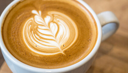 Latte art coffee cup with creamy milk foam design on wooden table, warm and inviting beverage for cozy moments