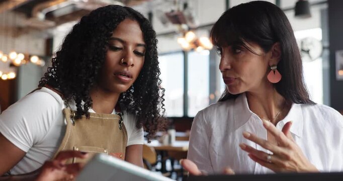 Women, waitress and conversation in cafe with tech for digital menu development, planning and feedback. People, manager and employee in coffee shop with tablet, laptop and discussion for hospitality.