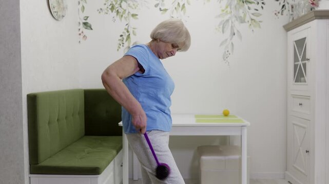Mature female carefully using specialized massage tool for targeting back and arm muscle groups, enhancing mobility and supporting independent wellness routine within comfortable home setting
