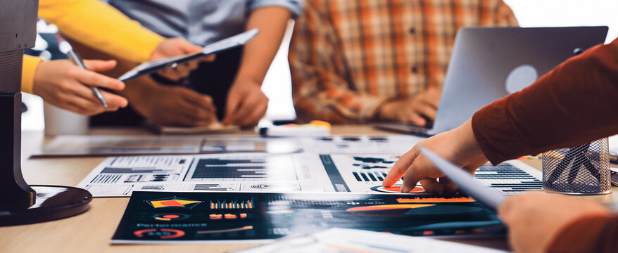 A diverse group of professionals collaborates in a modern office setting, analyzing data charts and graphs to develop effective business strategies through teamwork. SACTR