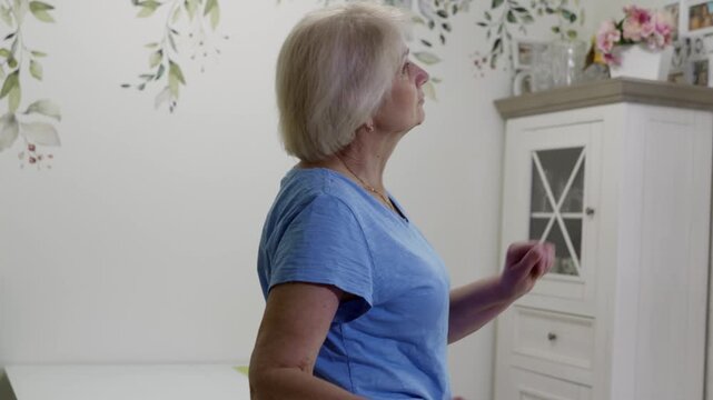 Mature woman wearing sportswear performing dynamic cardio movements in home environment, highlighting physical wellness and active senior lifestyle during retirement years