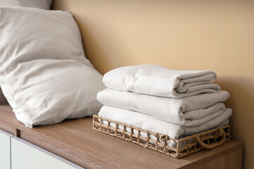 Commode with stack of clean bed sheets and pillow near beige wall in living room
