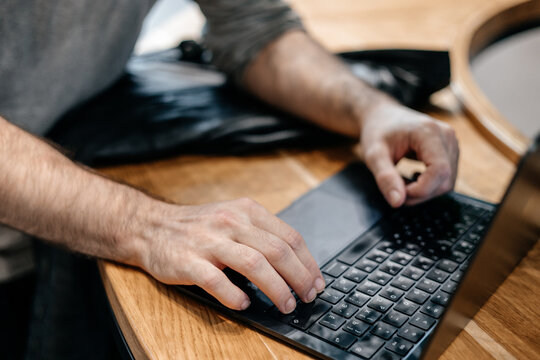 Close-up of a man’s hands typing on a laptop at a wooden desk in a modern workspace. Detail shot focusing on technology, remote work, and digital productivity