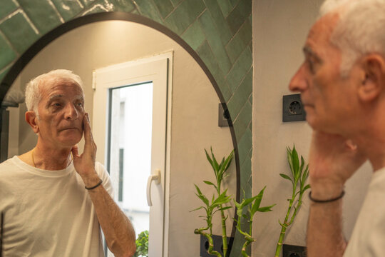 Senior man applying moisturizer to his face, reflecting self-care and morning routine