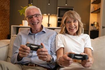 Senior couple laughing and playing video games on a sofa in their living room