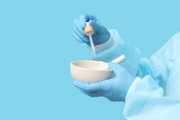 Young female scientist with mortar, pestle and pipette on blue background, closeup