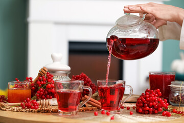 Young woman pouring hot viburnum tea from teapot into cup in living room, closeup